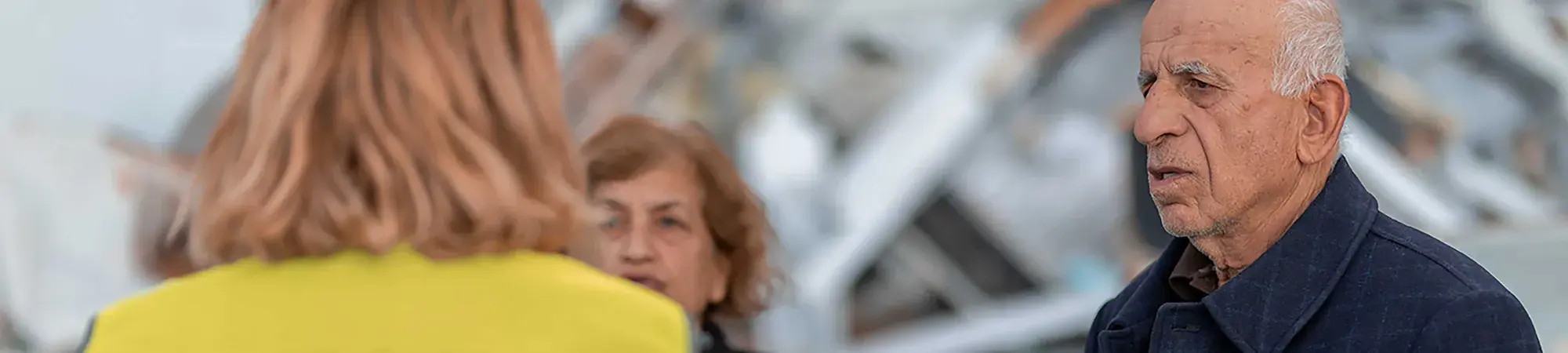 A man and woman talk to a volunteer in front of a pile of rubble.